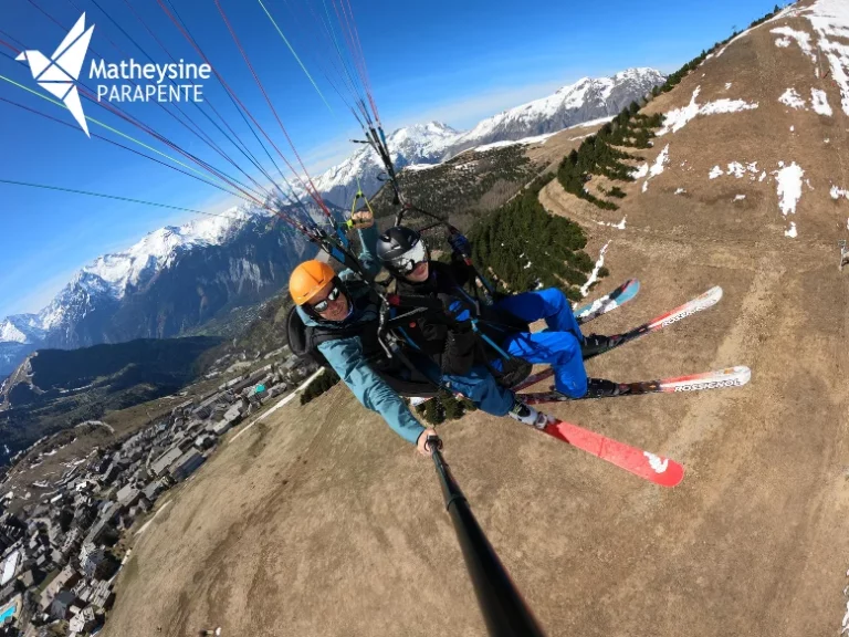Parapente biplace survolant la station de l'Alpe d'Huez avec une vue panoramique sur le village et les montagnes environnantes