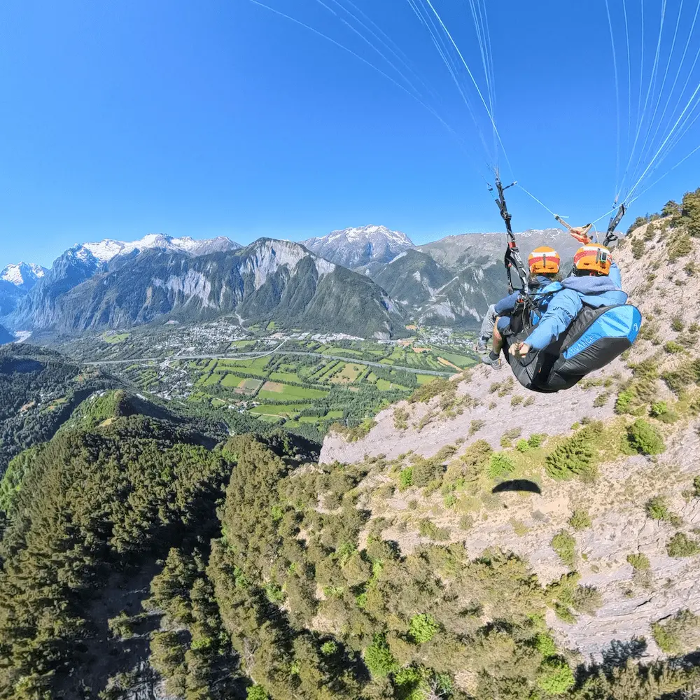 Vol parapente biplace face à la vallée de l’Oisans en été depuis l’Alpe d’Huez